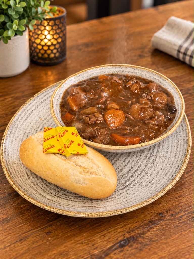 A bowl of stew with carrots, served with a bread roll and butter.
